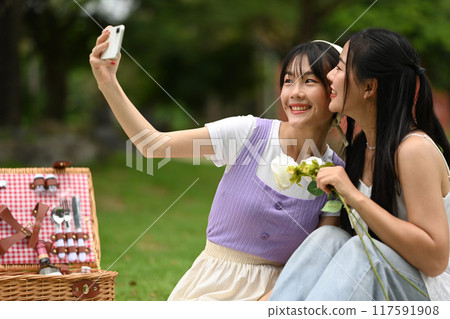 Affectionate lesbian couple taking selfie with smartphone during picnic in the park Affectionate lesbian couple taking selfie with smartphone during picnic in the park 117591908