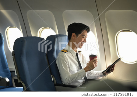 Young pilot drinking coffee and reading document on an airplane passenger seat Young pilot drinking coffee and reading document on an airplane passenger seat 117591913