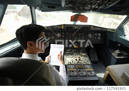 Back view of asian pilot dressed in a uniform preparing for flight in the cockpit of an aircraft 117591931