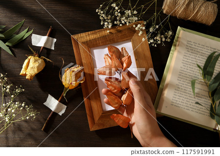 Dried flowers and plants, photo frame, book and hand on wooden background, top view 117591991