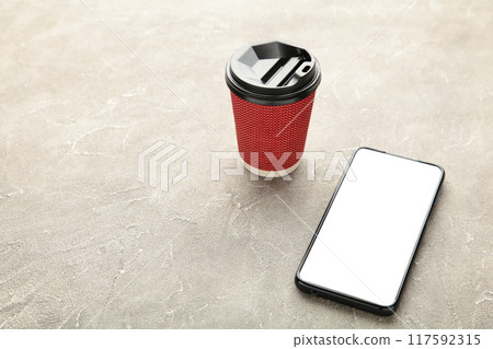 Black mobile smartphone with cup of coffee on grey background. Black mobile smartphone with cup of coffee on grey background. 117592315