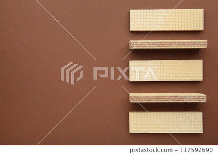 Tasty wafer sticks on brown background with copy space, flat lay. Sweet food Tasty wafer sticks on brown background with copy space, flat lay. Sweet food 117592690