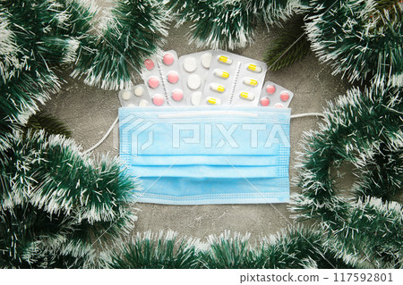 Medicine christmas new year concept during coronavirus covid time. Top view of medical pills with protective mask and fir-tree on grey background. Medicine christmas new year concept during coronavirus covid time. Top view of medical pills with protective mask and fir-tree on grey background. 117592801