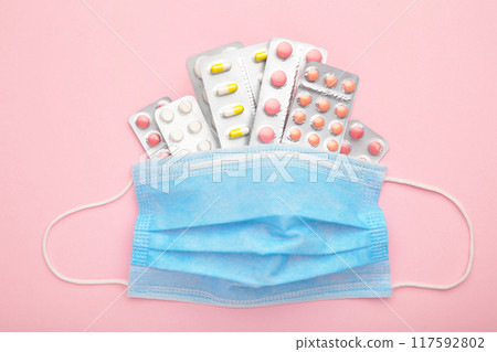 Protective face mask and pills, surgical mask on pink background. Coronavirus disease. 2019-nCoV Protective face mask and pills, surgical mask on pink background. Coronavirus disease. 2019-nCoV 117592802