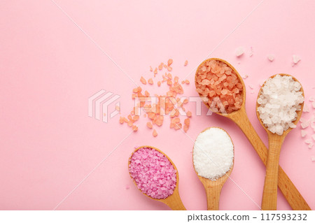 Various types of spa sea salt in wooden spoons on pink background 117593232