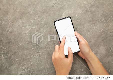 Woman hand holding the black smartphone with white screen on grey background. 117593736