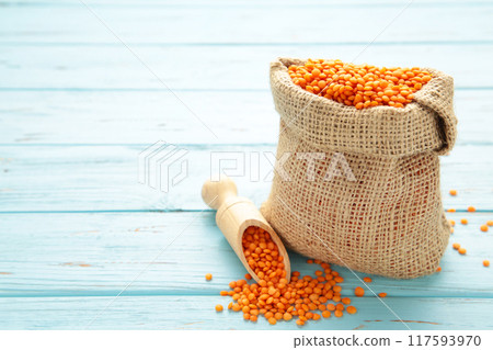 Red lentils in a wooden spoon and bag on blue wooden background. Red lentils in a wooden spoon and bag on blue wooden background. 117593970
