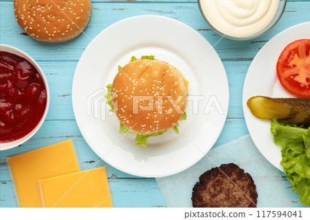 Burger in a white plate and ingredients on blue table. 117594041