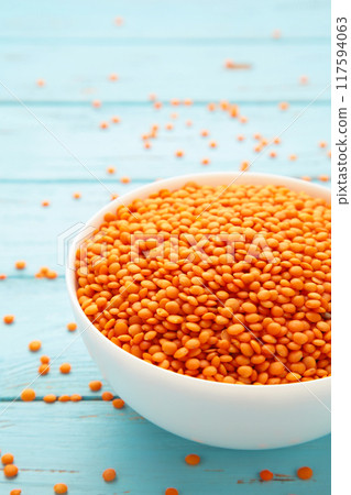 Red lentils in white bowl on a blue wooden table. 117594063
