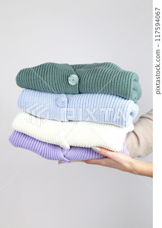 Stack of cozy knitted sweaters in hand on light background. Stack of cozy knitted sweaters in hand on light background. 117594067