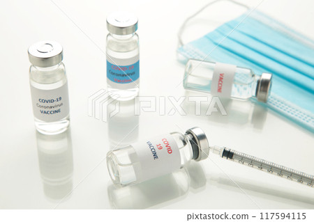 Coronavirus or COVID-19, 2019 - nCoV vaccine in a bottle with syringe and hygiene protective face mask on eflective surface. 117594115