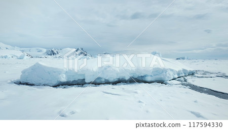 Massive snow covered iceberg in frozen ocean. Ice piece from crashed glacier towering Arctic coastline. Mountain range in background. Antarctica travel and exploration. Discover beauty of South Pole Massive snow covered iceberg in frozen ocean. Ice piece from crashed glacier towering Arctic coastline. Mountain range in background. Antarctica travel and exploration. Discover beauty of South Pole 117594330