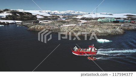 People travel to Antarctica. Explore South Pole. Tourists on red boat zodiac sailing polar ocean enjoy wild nature ocean landscape with snow covered mountains. Tourism expeditions. Aerial drone shot 117594377