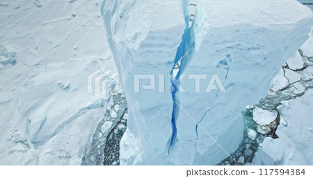 Blue high cracked iceberg towering in frozen Antarctica polar ocean. Huge snow covered ice glacier in wild nature environment icy landscape. Discover South Pole beauty. Aerial drone close up view 117594384