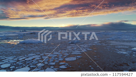 Arctic frozen ocean winter sunset landscape aerial view. Ice floes and snow covered icebergs under bright colorful evening sky. Antarctica travel and exploration. Discover the beauty of South Pole 117594427