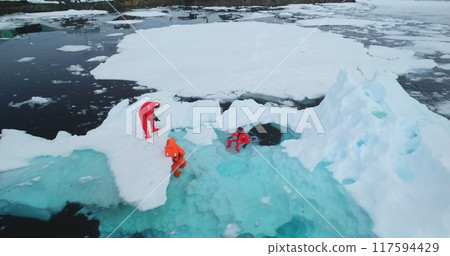 Science exploration on South Pole. People explore global warming in Antarctica. Group of scientists in orange wetsuits take samples and measure melting glacier water, climate change problem. Aerial 117594429