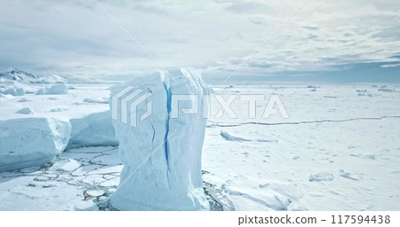 Calving iceberg from meted glacier with giant crack inside. Frozen ice covered ocean, mountains under moody blue sky. Cold winter landscape. Polar wild nature environment. Discover South Pole. Aerial 117594438