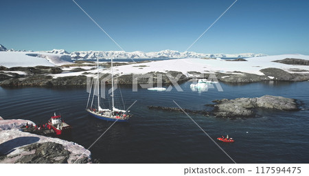 People travel Antarctica on yacht. Explore South Pole. Tourists on red boat zodiac sailing polar ocean enjoy wild nature landscape with snow covered mountains. Tourism expeditions. Aerial drone shot 117594475
