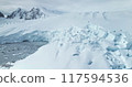 Giant calving glacier towering polar ocean in Antarctica. Snow covered blue iceberg ice wall rises above cold dark water. Antarctic winter landscape panorama. Aerial drone shot cinematic ecology scene 117594536