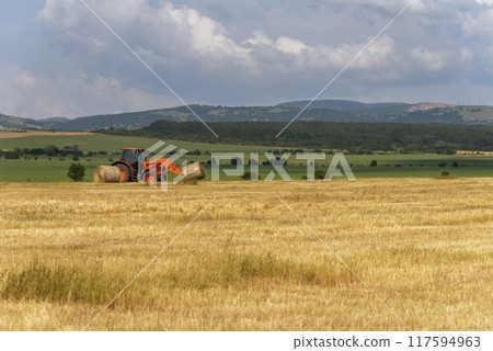 Tractor lifting hay bale on barrow. Tractor lifting hay bale on barrow. 117594963