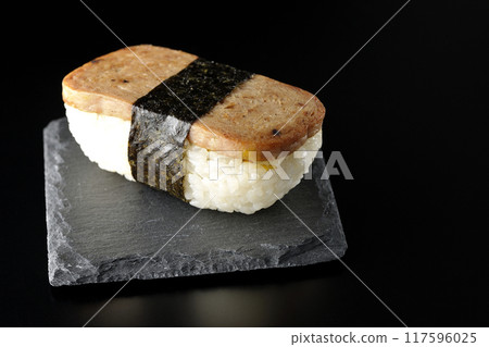 Spam musubi on a slate plate photographed against a black background 117596025