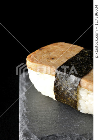 Spam musubi on a slate plate photographed against a black background 117596034