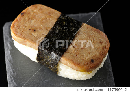 Spam musubi on a slate plate photographed against a black background 117596042