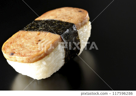 Spam musubi photographed against a black background 117596286