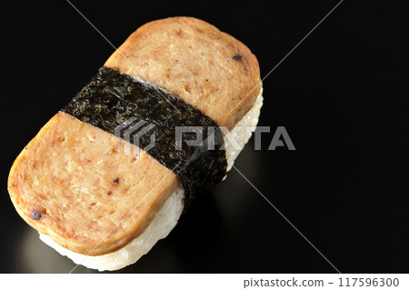 Spam musubi photographed against a black background 117596300