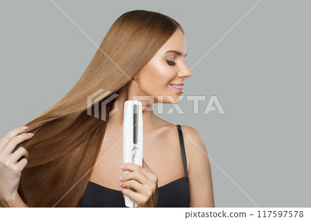 Profile of woman with hair straightener iron in studio isolated on white background.  117597578