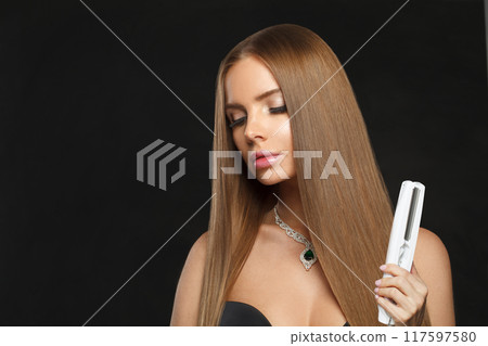 Good-looking woman with long hair using a straight hair iron and doing a hairstyle 117597580