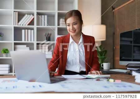 woman meticulously plans a finance audit, using a computer and calculator to review budget documents and ensure accuracy 117597928