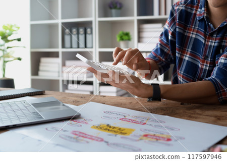man meticulously plans a finance audit, using a computer and calculator to review budget documents and ensure accuracy. 117597946