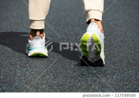 Athlete legs in white sneakers with hard shadow stand on blue outdoor sports playground. Back view. Workout. Close up. Outdoors. Athlete legs in white sneakers with hard shadow stand on blue outdoor sports playground. Back view. Workout. Close up. Outdoors. 117599500