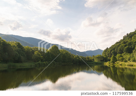 Mountain lake with perfect reflection at sunrise. Calmness landscape with cloudy sky, hills, forest. Mountain lake with perfect reflection at sunrise. Calmness landscape with cloudy sky, hills, forest. 117599536