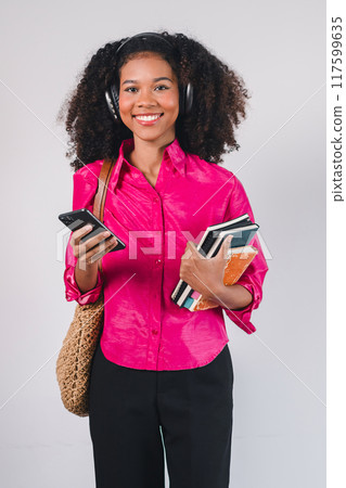 Smiling African American woman holding a smartphone and books. Isolated on white background. 117599635