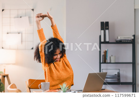 African American woman stretching her arms while taking break from working on laptop at home. 117599671