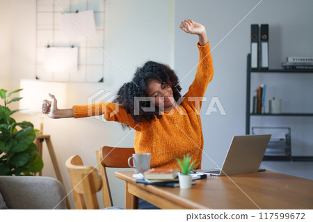 African American woman stretching her arms while taking break from working on laptop at home. 117599672