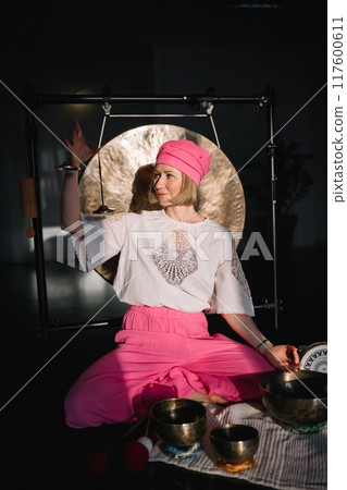 Close-up view of woman using singing bowl in sound healing therapy indoors.  117600611