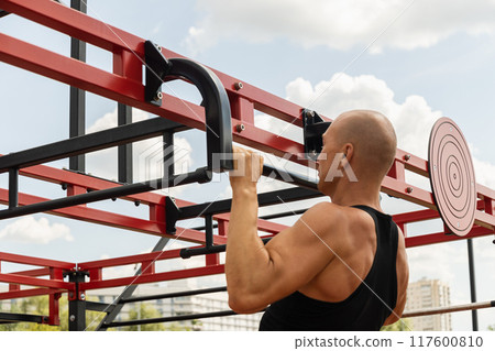 Athlete muscular fitness male pulling up on horizontal bar at street gym. Outdoors. Summer. Workout routine. Athlete muscular fitness male pulling up on horizontal bar at street gym. Outdoors. Summer. Workout routine. 117600810