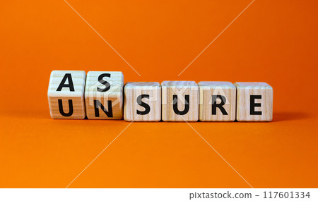 Assure or unsure symbol. Turned wooden cubes and changed the concept word unsure to assure. Beautiful orange table, orange background, copy space. Business and assure or unsure concept. 117601334