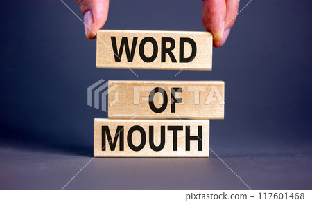 Word of mouth symbol. Concept words Word of mouth on wooden blocks on a beautiful grey table grey background. Businessman hand. Business, finacial and word of mouth concept. Copy space. 117601468