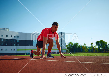 Low angle photo of young man, ready to run standing on start line in low start position. Achievements and motivation. 117601489