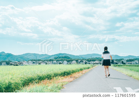 穿著水手服、綁著辮子的女孩沿著夏日稻田路奔跑 穿著水手服、綁著辮子的女孩沿著夏日稻田路奔跑 117601595
