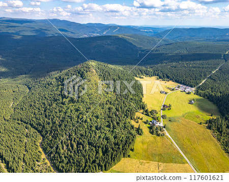 Aerial view of Bukovec Mountain, surrounded by lush forests and fields, overlooking the picturesque Jizerka village in the Jizera Mountains on a clear day. 117601621