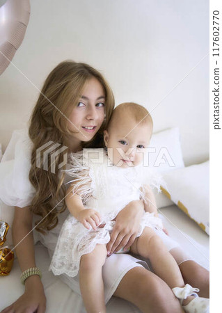 a        photo session on the first birthday of a baby girl with her  teenage sister, in pastel colors, minimalism 117602770