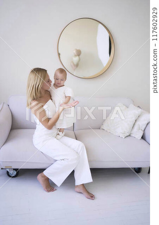 mother with a baby girl in a stylish white minimalist interior in white clothes 117602929
