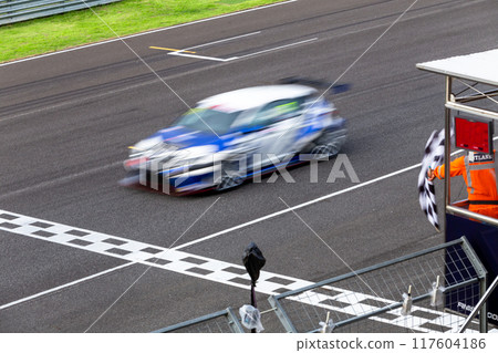 Race car crossing finish line on track and pass checkered race flag, Checkered racing finish flag with Race car crossing the finish line on circuit. 117604186