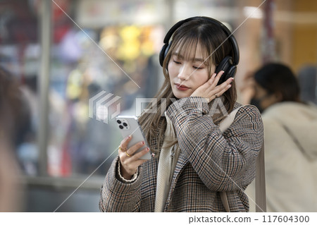 一位戴著耳機、拿著智慧型手機的年輕女子 117604300