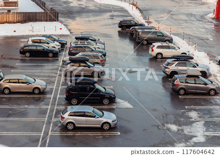 View from above on car parking with many vehicles and free lots at bright early frosty cold winter morning. Parking lot with snowdrifts near airport terminal or shopping business mall at cold weather 117604642